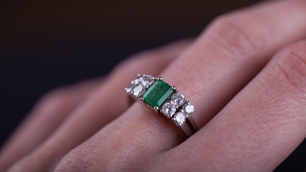 Close up of an emerald ring in woman finger, with diamonds and platinum. Studio shot, black background.
