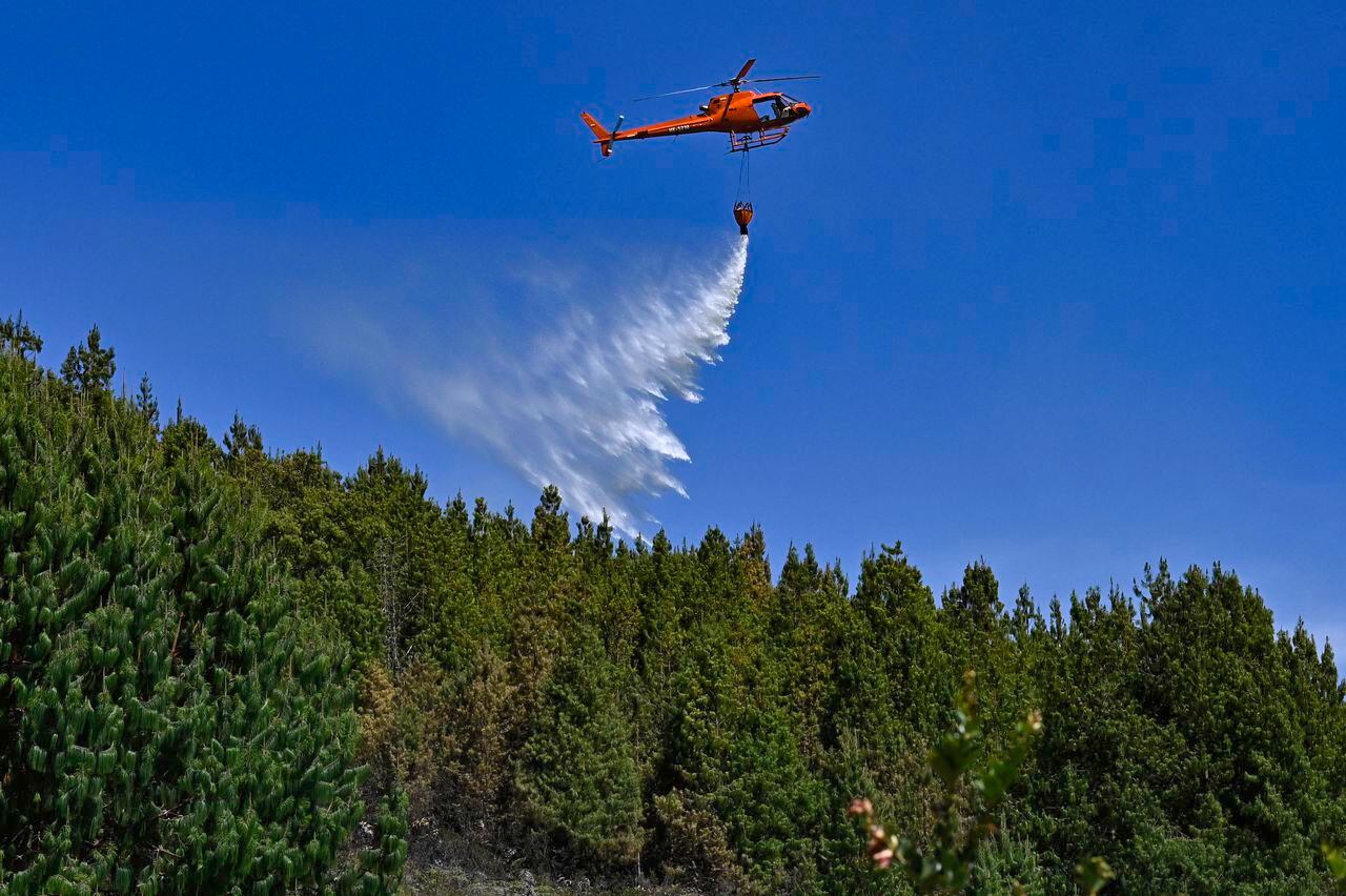 A helicopter drops water to put out a forest fire in Nemocon, Colombia on January 26, 2024. Yesterday Colombia asked the member countries of the United Nations for help to extinguish around thirty forest fires that are ravaging several regions and drowning the capital, Bogota, in smoke. (Photo by Luis ACOSTA / AFP)