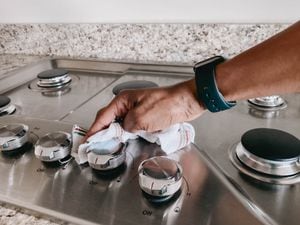 Close-up of woman's hand wiping down cooktop with wet dishcloth