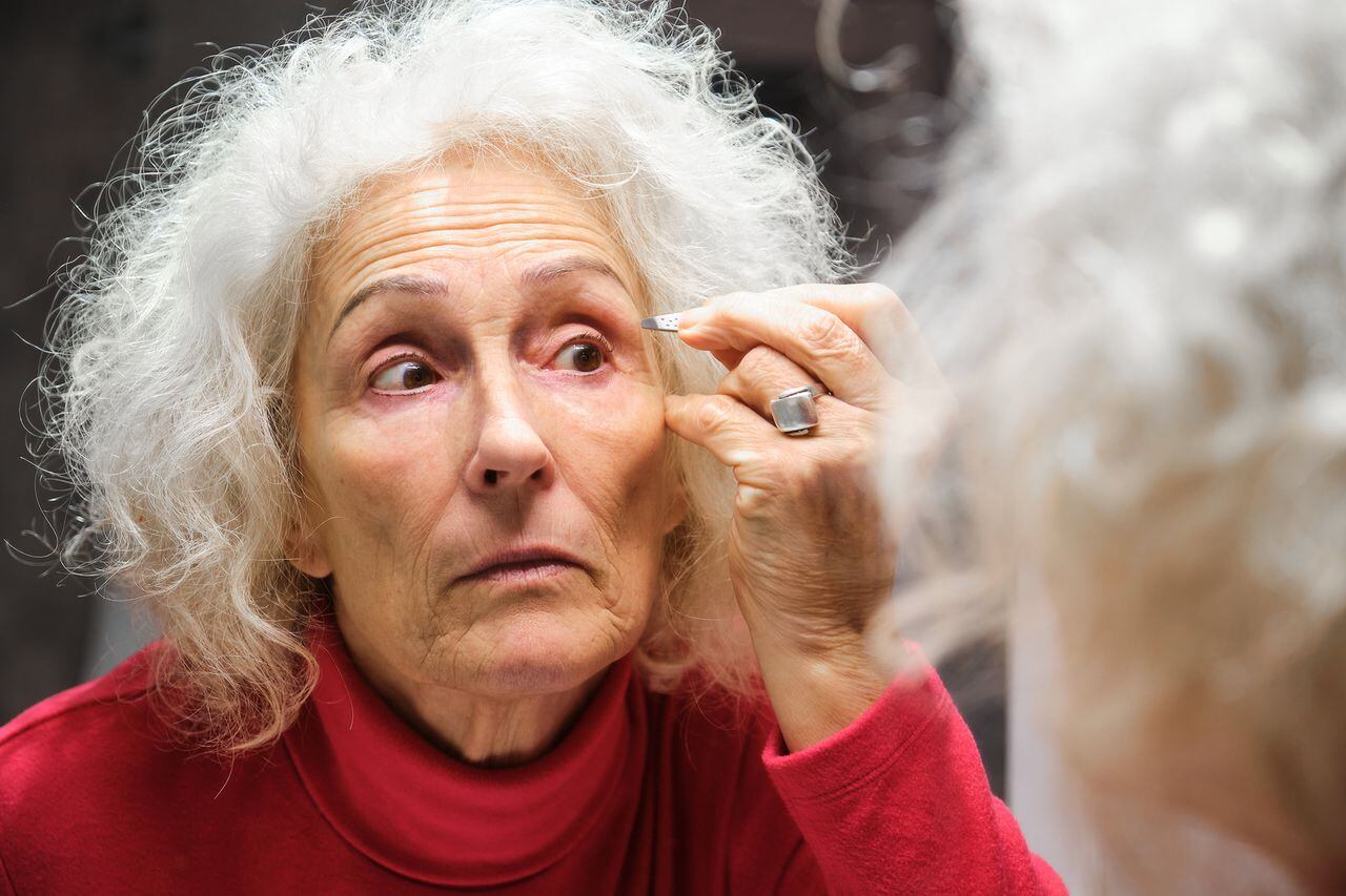 Senior Hispanic woman depilating her eyebrows with tweezers.
