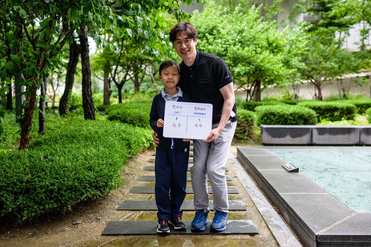 En esta foto tomada en Seúl el 21 de junio de 2023, Yoon Jae-ha (izquierda) posa con una pizarra que muestra su edad internacional, 8 años, y su edad coreana, 9, junto a su padre, Yoon Dong-gun, que trabaja en comercio, y cuya edad internacional es 43 y coreana 44.