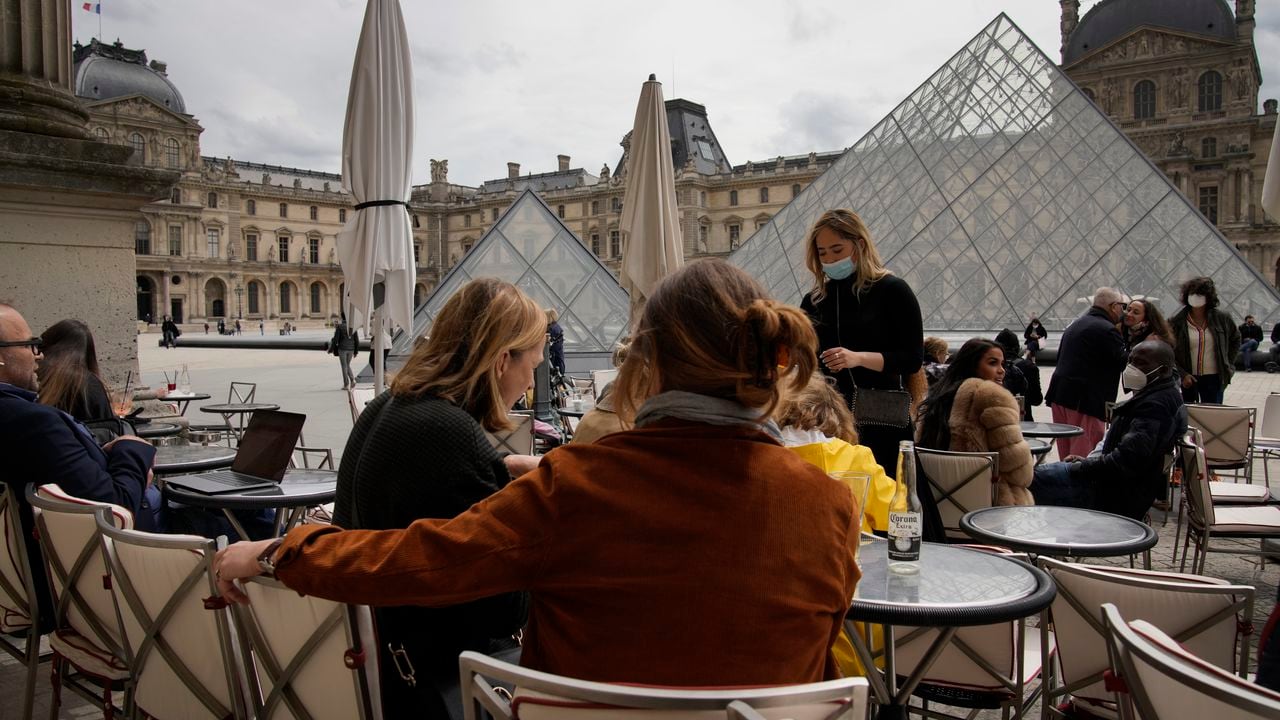 La gente toma un café al aire libre en un bar frente al museo del Louvre en París, el jueves 20 de mayo de 2021. AP Photo/Christophe Ena
