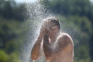 25 de junio de 2023, Baden-Württemberg, Ertingen: Un hombre se refresca bajo una ducha en Schwarzachtalsee