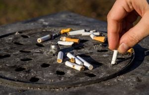 Close up picture of dirty street ashtray with a hand extinguishing cigarette at smoking area.
Hand putting out a cigarette.