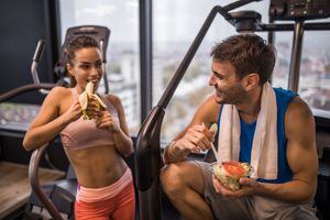 Happy athletes communicating while eating healthy food on a break in a health club. Focus is on man.