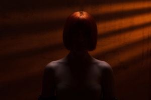 silueta de una misteriosa mujer pelirroja con los hombros descubiertos, retrato de una niña de incógnito, niña desnuda irreconocible contra una pared con rayos naranjas, concepto de criminal, violencia, secreto