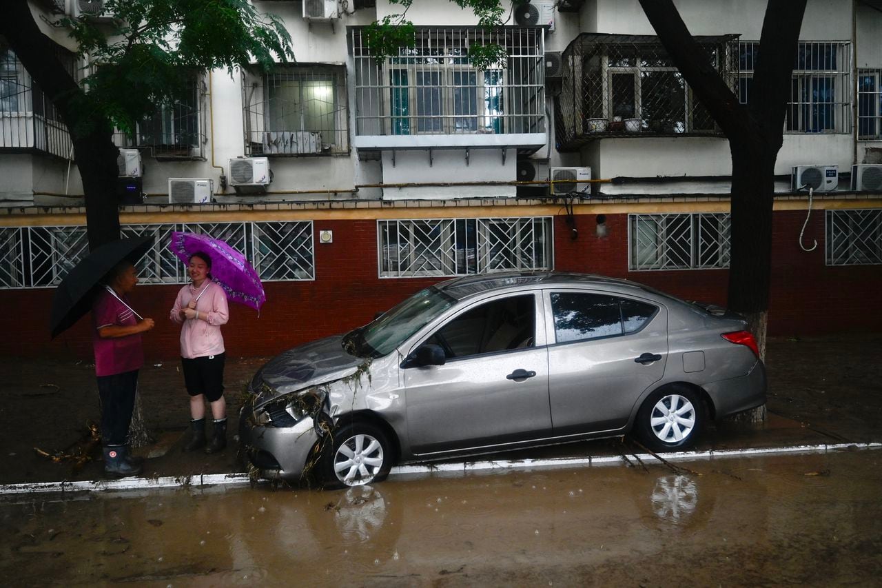 Locals stand along a flooded street after heavy rains in Mentougou district in Beijing on July 31, 2023. Heavy rains battered northern China on July 31, killing at least two people in Beijing while washing away cars and inundating subway stations, with the capital issuing its highest alerts for flooding and landslides. (Photo by Pedro PARDO / AFP)