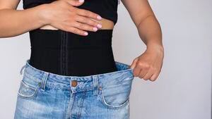 A woman fastens a corset for figure correction. A black belt that tightens the stomach and waist. The concept of excess weight .