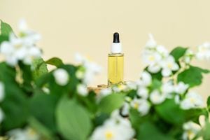 Natural cosmetic product, serum or oil for the care of skin and hair with jasmine flowers on beige background. Organic, bio cosmetics concept. Natural skincare bottle with serum.