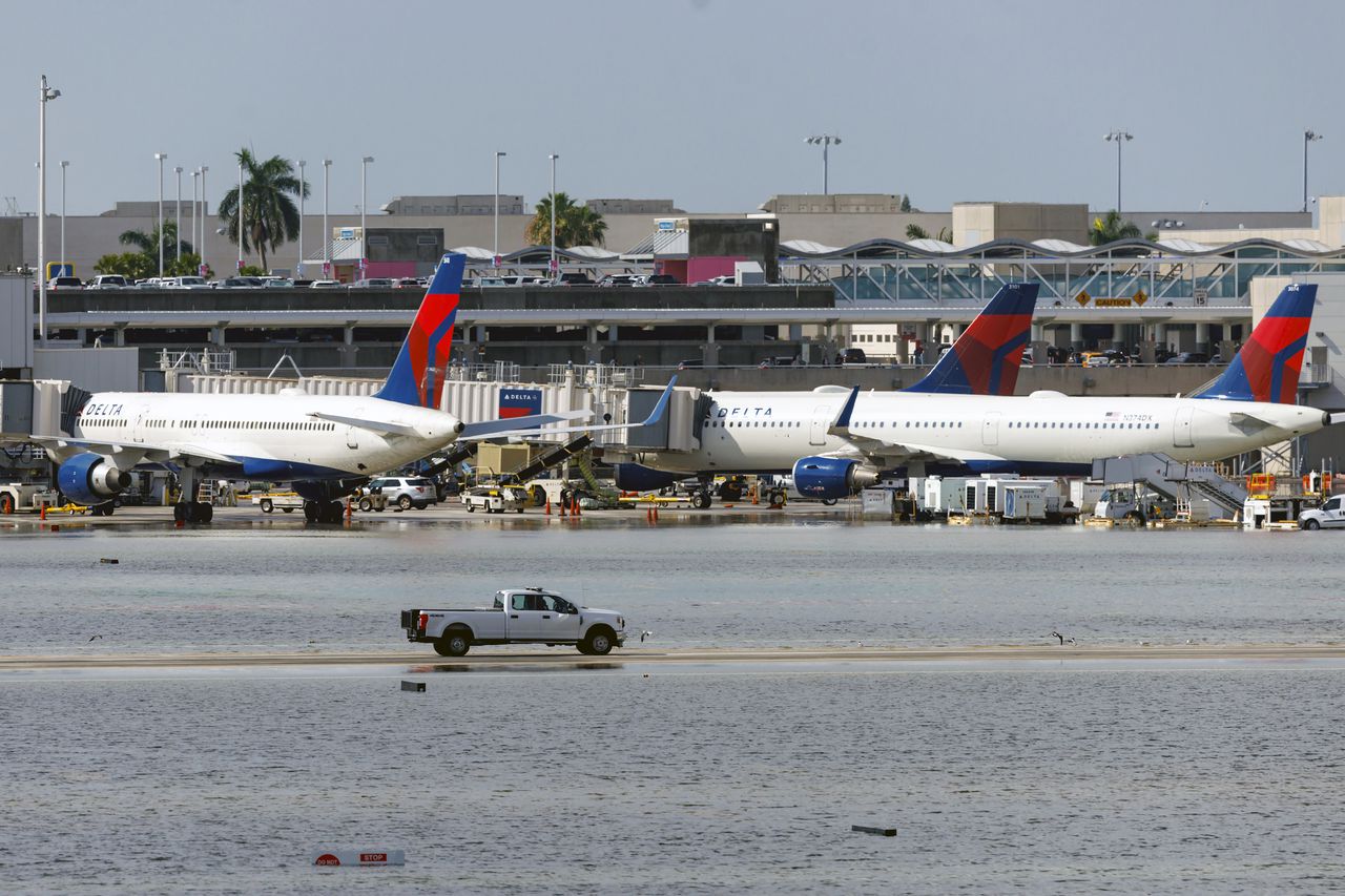 Aviones de Delta Air Lines en su terminal mientras un camión atraviesa la pista inundada del Aeropuerto Internacional de Fort Lauderdale-Hollywood
