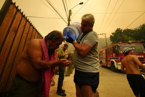 A man helps a fellow resident cool down with bottled water as forest fires burn nearby, in Vina del Mar, Chile, Saturday, Feb. 3, 2024. Officials say intense forest fires burning around a densely populated area of central Chile have left several people dead and destroyed hundreds of homes. (AP Photo/Esteban Felix)