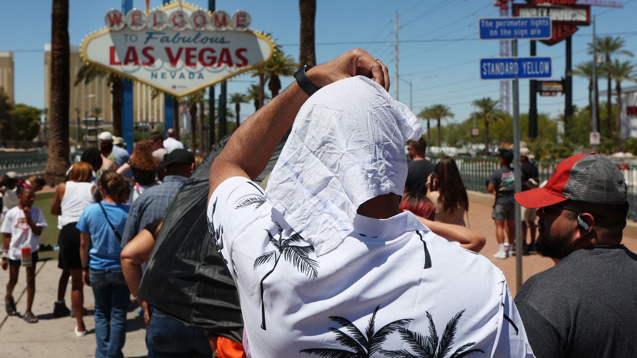 Hombre se protege del sol mientras espera en la fila para tomar una foto en el histórico cartel de Bienvenido a Las Vegas durante una ola de calor en Las Vegas, Nevada, el 14 de julio de 2023.