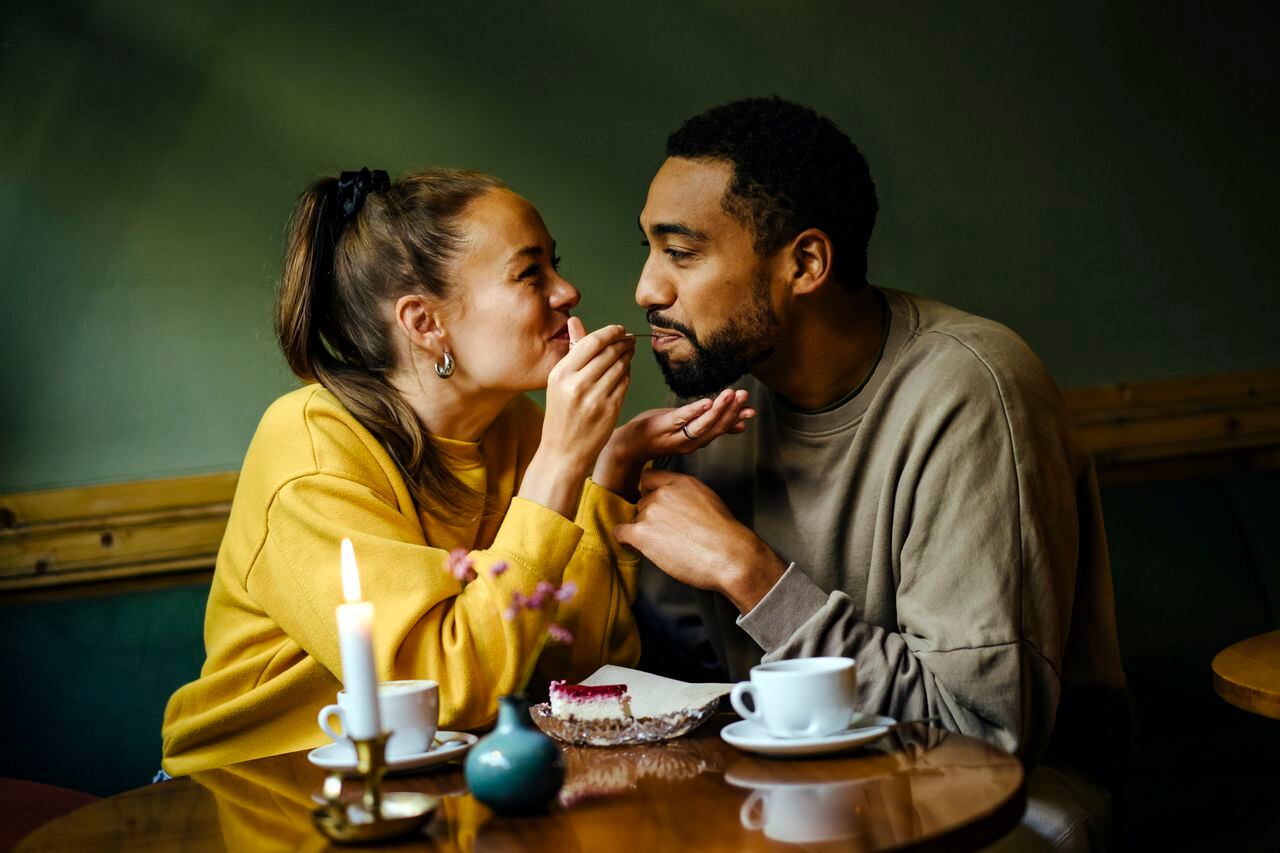 Girlfriend feeding bite of raspberry cheesecake to her boyfriend at coffee shop