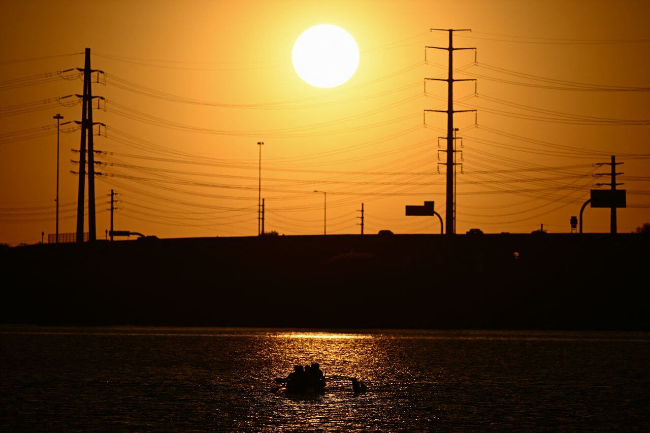 El sol se pone detrás de las líneas eléctricas mientras la gente rema en Tempe Town Lake durante una ola de calor récord en Tempe, Arizona, el 18 de julio de 2023.