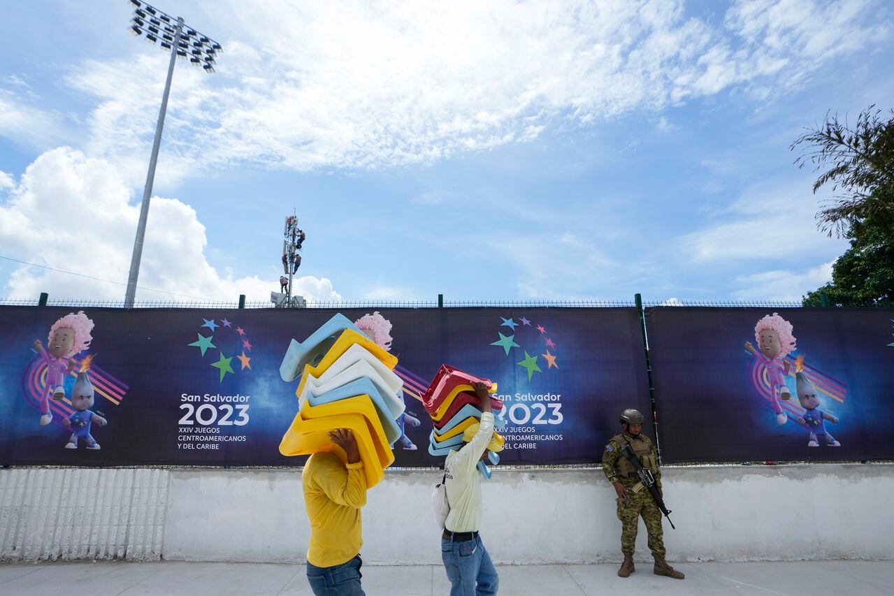 Dos trabajadores cargan butacas a ser instaladas en el Estadio Mágico González de San Salvador, el jueves 22 de junio de 2023, a un día de la inauguración de los Juegos Centroamericanos y del Caribe (AP Foto/Arnulfo Franco)