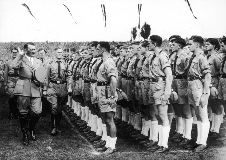 Adolf Hitler y Rudolf Hess saludan a las juventudes hitlerianas en 1938. Wikimedia Commons
