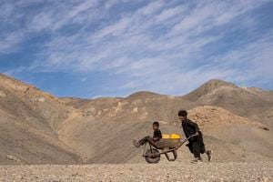 Un niño empuja una carretilla con bidones y su hermano menor, en su camino a recoger agua de una piscina estancada, a unos 3 kilómetros (2 millas) de su casa en la aldea de Kamar Kalagh en las afueras de Herat, Afganistán, el viernes 26 de noviembre de 2021. La sequía de Afganistán, la peor en décadas, está entrando ahora en su segundo año, agravada por el cambio climático. Foto AP / Petros Giannakouris