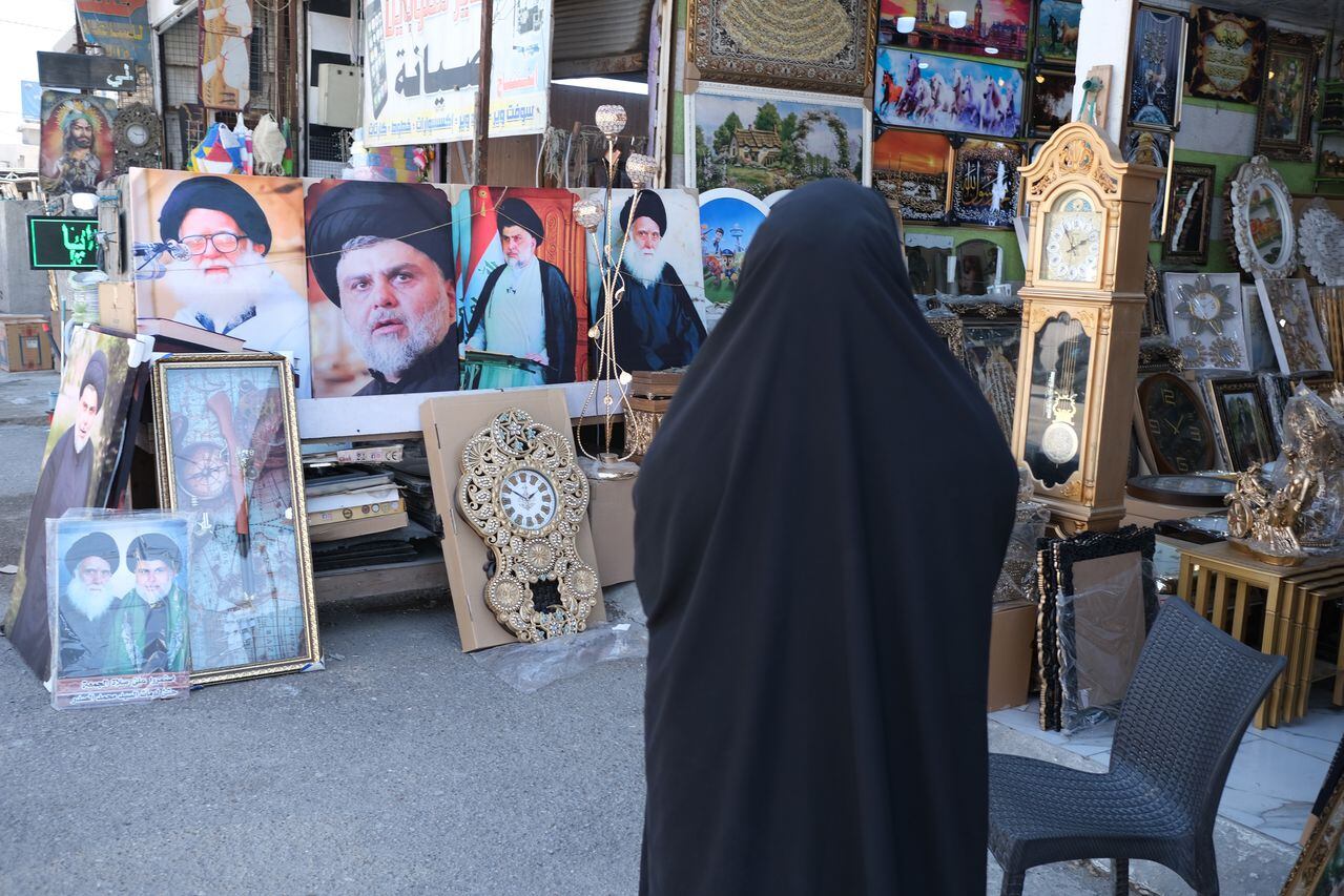 Una mujer con chador negro se para frente a carteles de los grandes ayatolás iraquíes fallecidos en Ciudad Sadr el 18 de marzo de 2023 en Bagdad, Irak. Ciudad Sadr es el bastión de Muqtada al-Sadr, un clérigo chiita, político iraquí y líder de la milicia.
