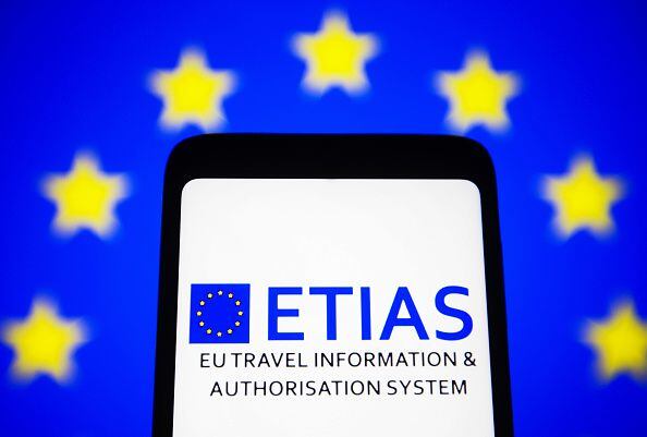 El logotipo del Sistema Europeo de Información y Autorización de Viajes (ETIAS) en la pantalla de un teléfono inteligente y la bandera de la UE (Unión Europea) al fondo.