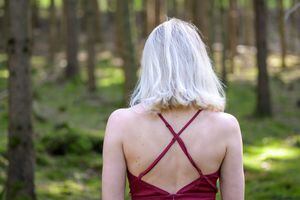 Rear view of woman with medium-length blond hair wearing backless magenta dress in forest