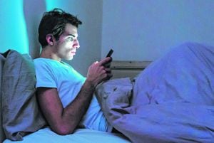 Un joven a oscuras en altas horas de la noche mirando su celular.