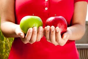 Asian woman holds a red delicious apple and a green granny smith apple