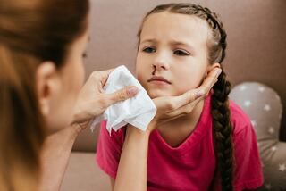 cropped view of mother holding napkin near daughter with nasal bleeding