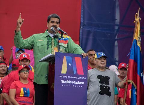 la ex estrella del fútbol argentino Diego Maradona (R) sostiene la bandera venezolana mientras el presidente venezolano, Nicolás Maduro, pronuncia su último discurso de campaña.