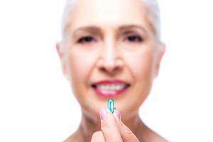 selective focus of attractive smiling senior woman with pill, isolated on white