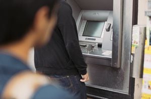 Man using a bank atm machine on the street with a thief watching him from behind