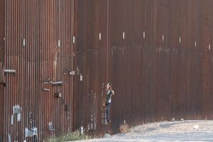 Un traficante de personas explora a través del muro fronterizo para asegurarse de que la patrulla de la frontera no esté cerca para enviar migrantes a EE. UU. desde México.