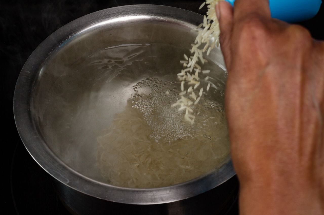 Rice being poured from a measuring cup into hot water to boil / cook