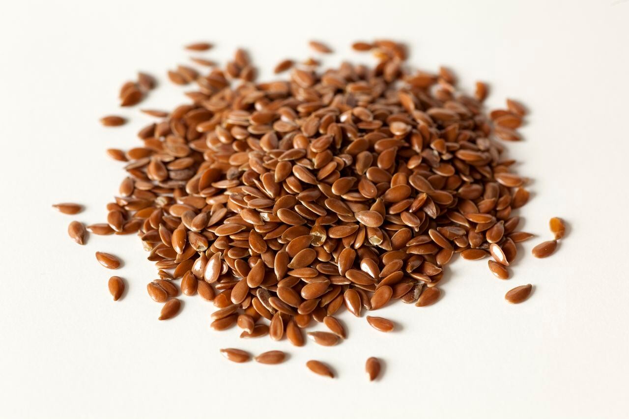 A close up of a pile of dries flax seeds on a white background.