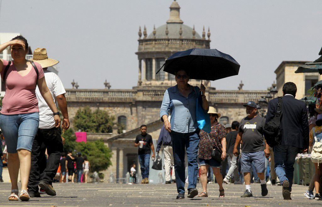A group of people try to protect themselves from the intense sun during one of the hottest days of the third heat wave earlier this week that will see temperatures soar to levels normally not seen in Guadalajara, Jalisco state, Mexico on June 12. , 2023. (Photo by ULISES RUIZ / AFP)