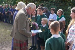 La reina Camilla de Gran Bretaña (L) y el rey Carlos III de Gran Bretaña (2L) reciben flores y una tarjeta de los niños de las escuelas locales cuando salen después de asistir a un servicio religioso en el pueblo de Crathie, cerca de Balmoral en el centro de Escocia.