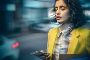 An Asian/Indian young adult businesswoman feels dizzy at night on a busy road because of the heavy use of a smartphone on the go.