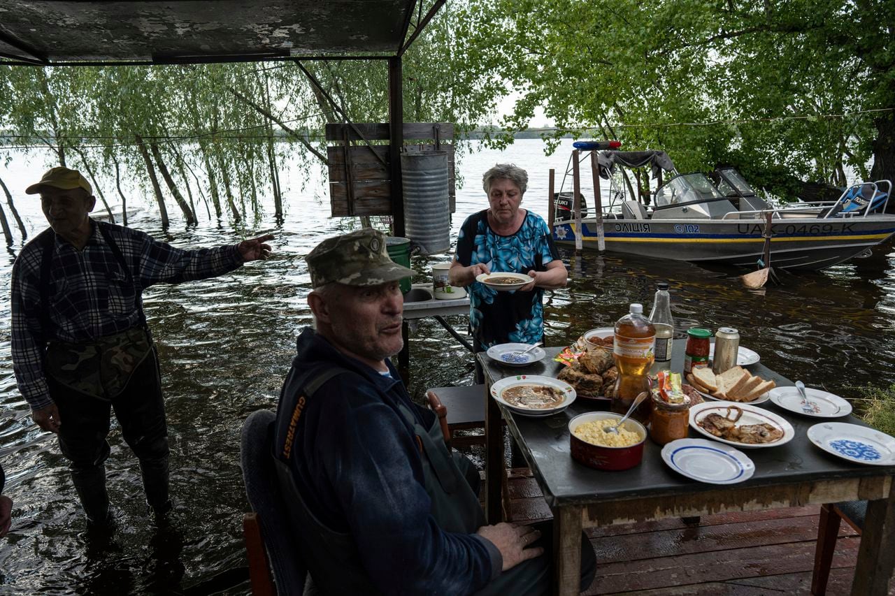 Lyudmila Kulachok, de 54 años, a la derecha, pone la comida en la mesa para la cena familiar en el patio inundado de su casa en la isla del embalse de Kakhovka en el río Dnipro cerca de Lysohirka, Ucrania, el jueves 18 de mayo de 2023.
