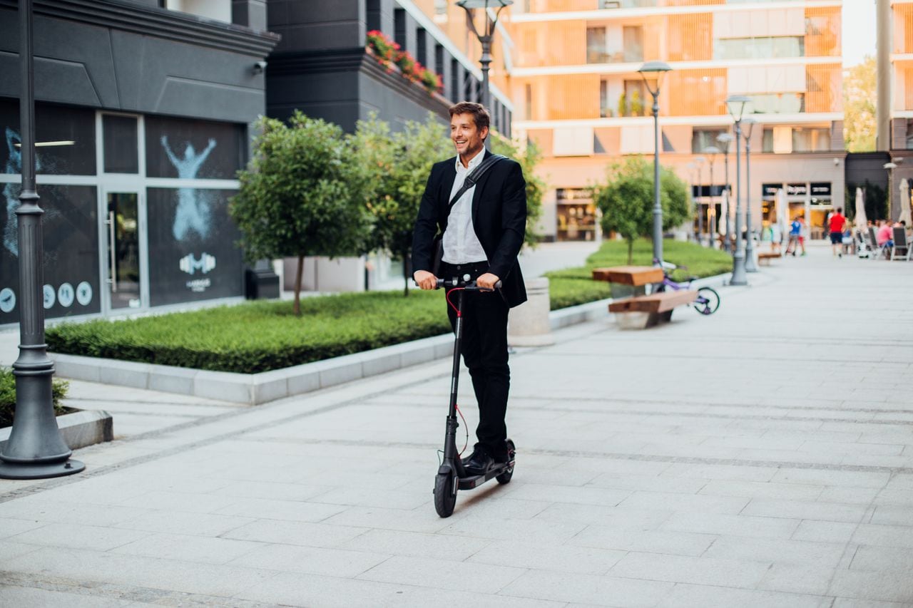 Hombre de negocios en un traje que monta patineta eléctrica. Transporte, movilidad.