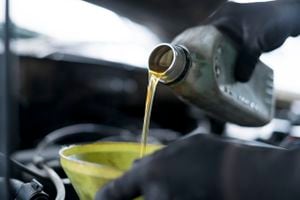 Primer plano del mecánico de automóviles manual que reposta combustible y vierte aceite, llena el aceite en el motor, el mantenimiento y el rendimiento en el taller de reparación de automóviles.