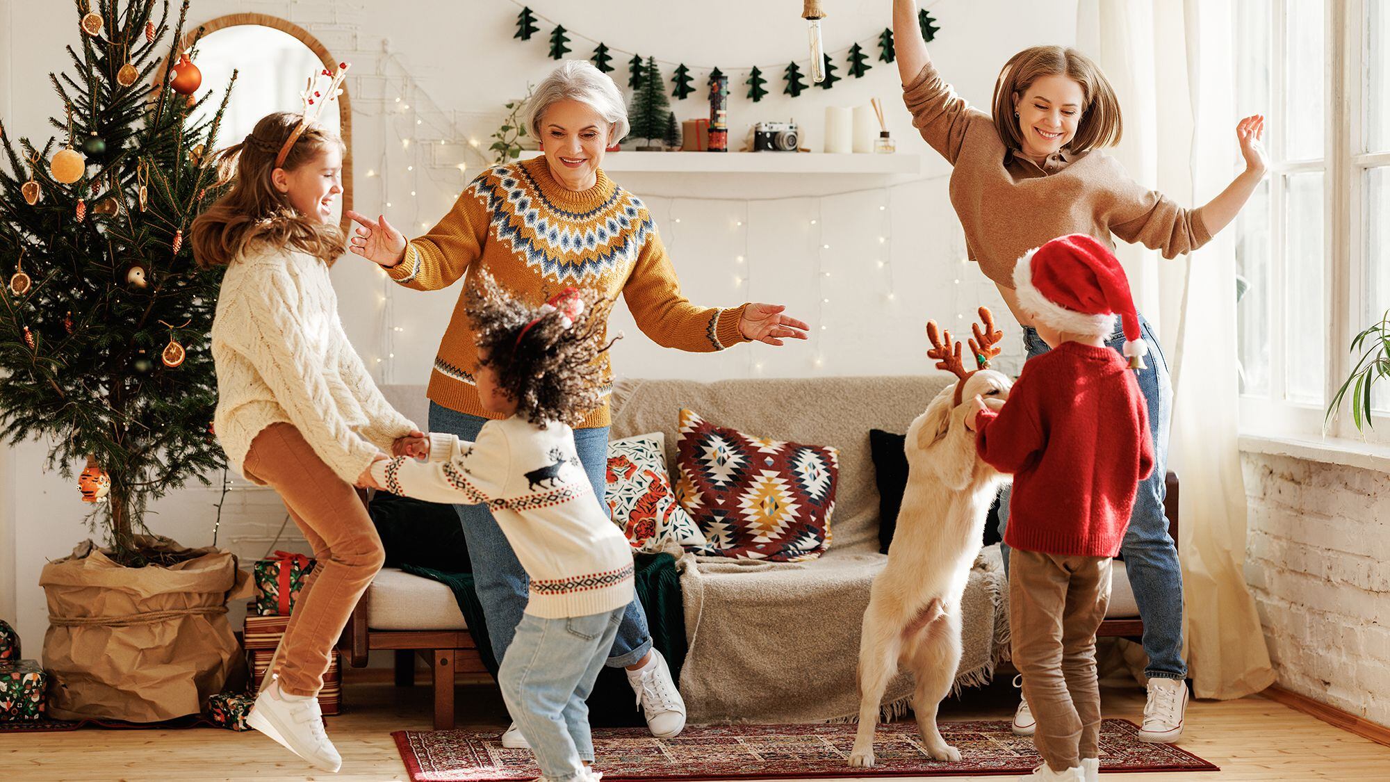 Feliz familia multirracial positiva con tres hijos y golden retriever divertirse el día de Navidad en casa. Madre, abuela y niños multiétnicos bailan con música de Año Nuevo durante las vacaciones de invierno
