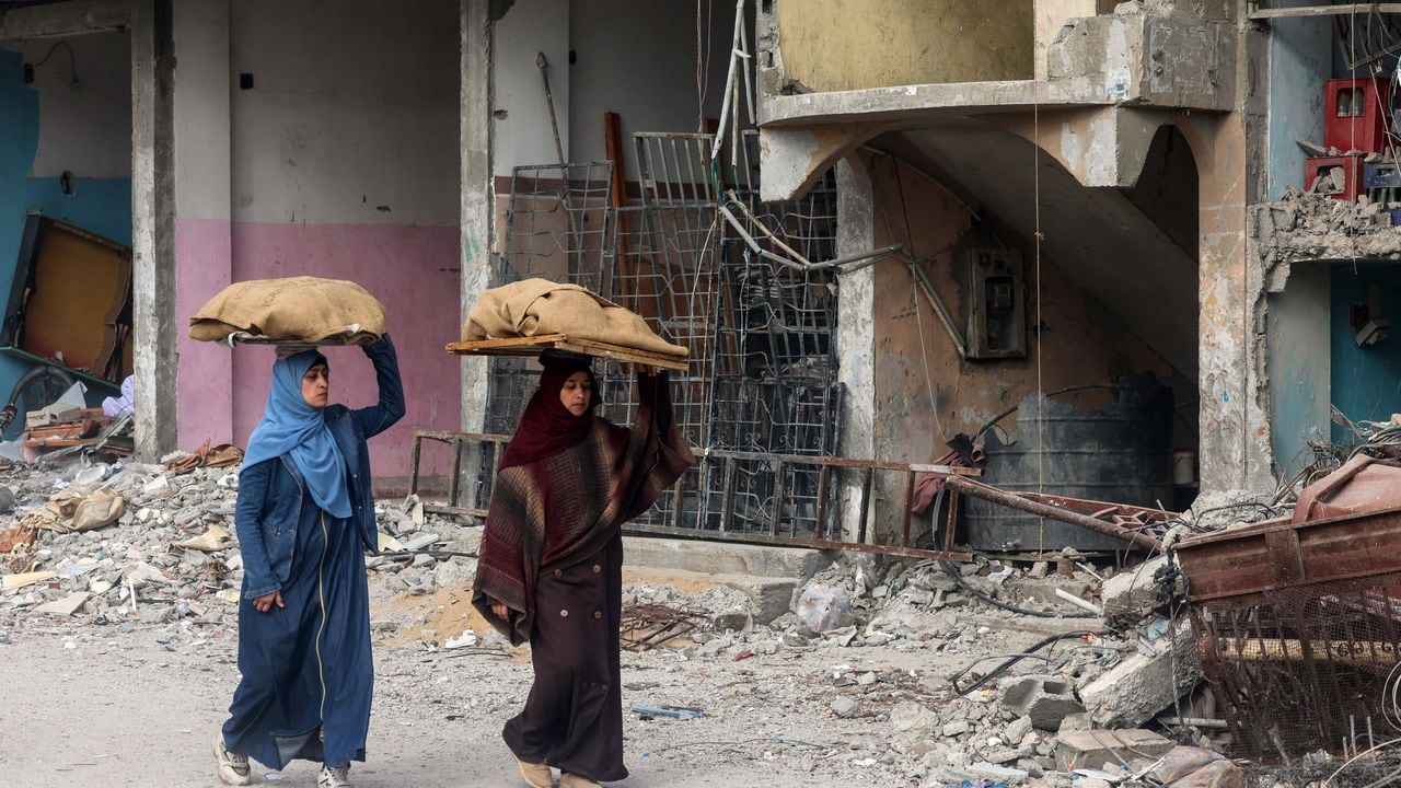 Las mujeres llevan hogazas de pan sobre sus cabezas mientras caminan frente a un edificio dañado por el bombardeo israelí en Rafah, en el sur de la Franja de Gaza, el 25 de febrero de 2024, en medio de continuas batallas entre Israel y el grupo militante palestino Hamas. (Foto de MOHAMMED ABED / AFP)
