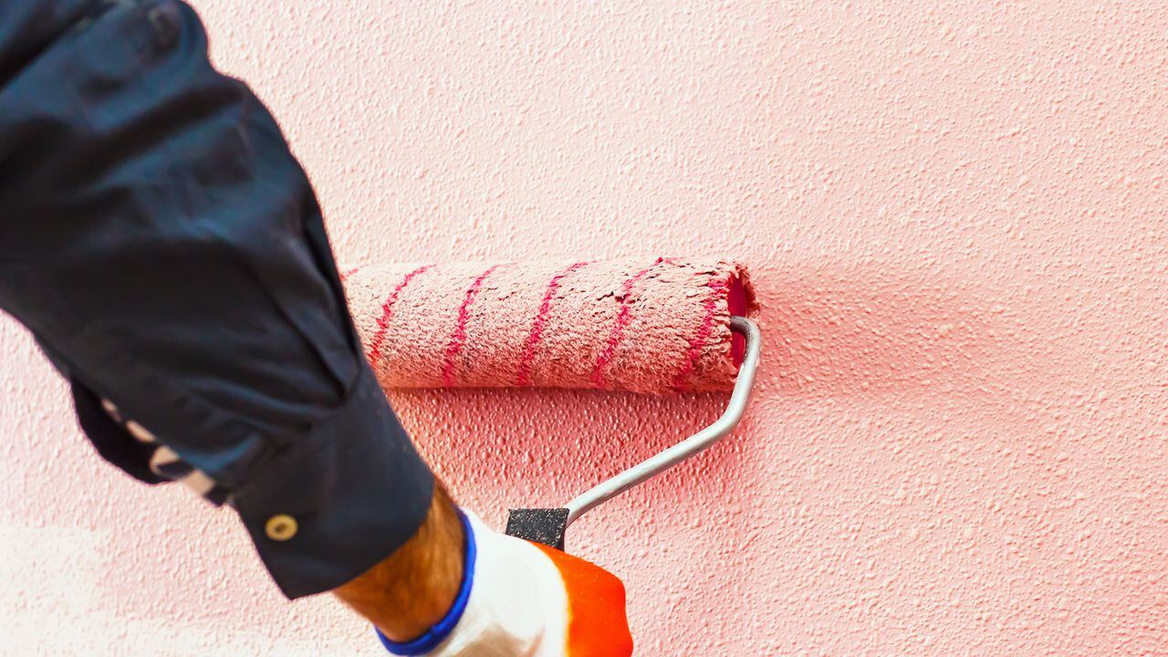 Hombre pinta la pared a mano con un rodillo de pintura mientras se trabaja en interiores, hacer reparaciones