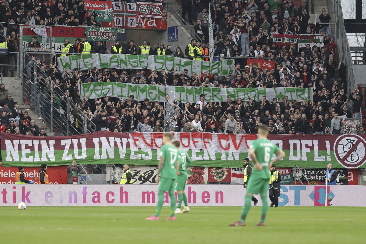 Los fanáticos de Augsburgo sostienen pancartas que dicen "Cuánto dura 50+1 todavía depende de nosotros" y "No a los inversores en la DFL" durante el partido de fútbol de la Bundesliga alemana entre Augsburgo y Mainz, en Mainz, Alemania, el sábado 17 de febrero de 2024. (Jürgen Kessler/dpa vía AP)