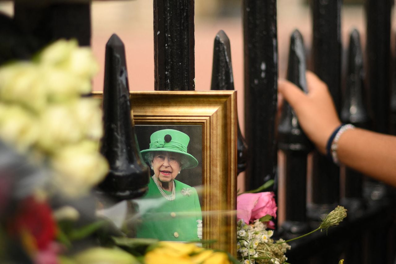 Una fotografía enmarcada de la reina Isabel II de Gran Bretaña se ve en las rejas del Palacio de Buckingham en el centro de Londres el 8 de septiembre de 2023, mientras los simpatizantes conmemoran la vida de Su difunta Majestad la Reina Isabel II en el primer aniversario de su fallecimiento. (Foto de Daniel LEAL / AFP)