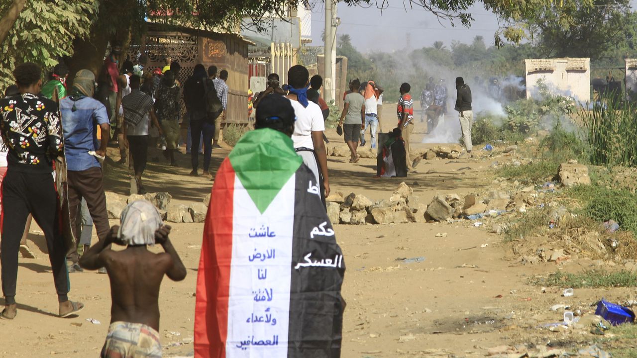Un hombre envuelto en una bandera de Sudán observa cómo las fuerzas de seguridad sudanesas disparan gases lacrimógenos contra los manifestantes durante una manifestación que pide un gobierno civil y denuncia la administración militar, en la ciudad gemela de Umdurman, la capital de Jartum, el 30 de noviembre de 2022.
