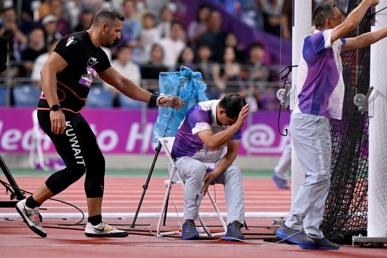 In this picture taken on September 30, 2023, an official reacts in pain after his leg was injured by a stray hammer thrown by Ali Zankawi (L) who attempts to stem the bleeding during the men's hammer throw final athletics event at the 2022 Asian Games in Hangzhou in China's eastern Zhejiang province. (Photo by William WEST / AFP)