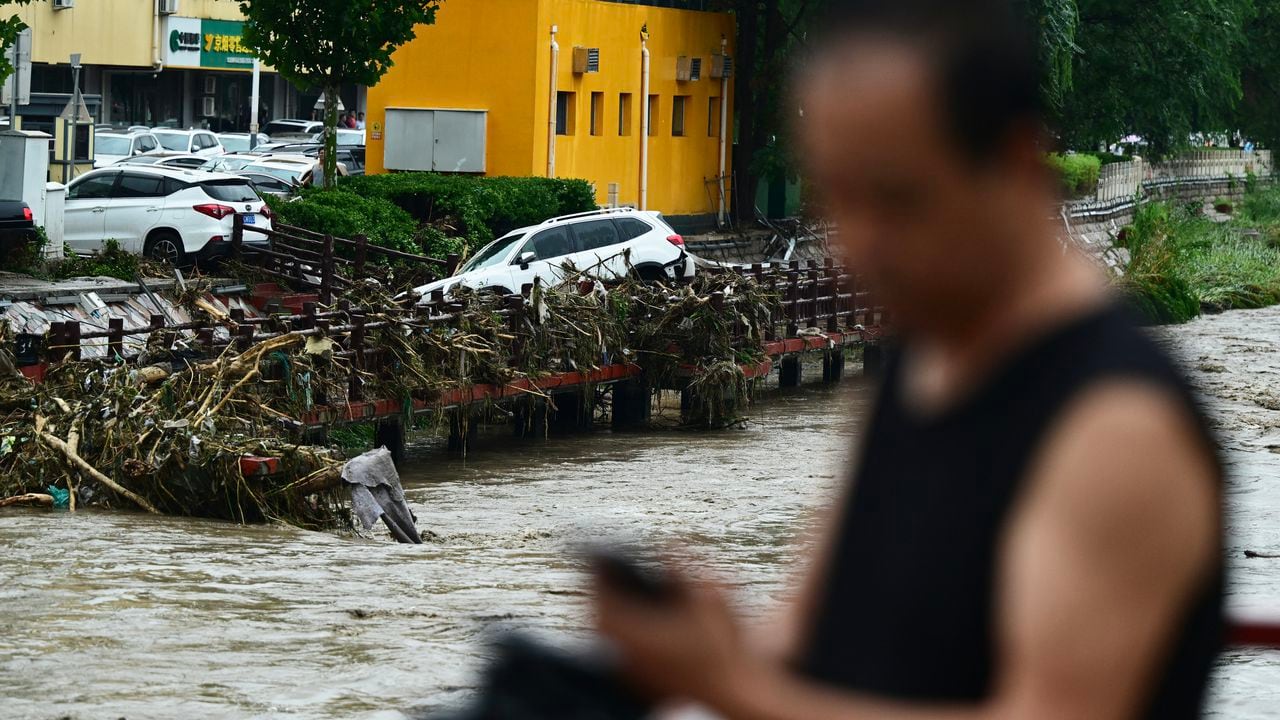 A man stands by the overflooded Yongding river, after heavy rains in Mentougou district in Beijing on July 31, 2023. Heavy rains battered northern China on July 31, killing at least two people in Beijing while washing away cars and inundating subway stations, with the capital issuing its highest alerts for flooding and landslides. (Photo by Pedro PARDO / AFP)