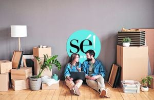 Young couple sitting in new apartment surfing Internet on laptop searching for interior design pictures and choosing one