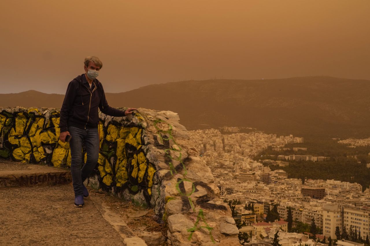 Un hombre con una máscara camina por la colina de Licabeto mientras se ve la ciudad de Atenas al fondo, el martes 23 de abril de 2024.