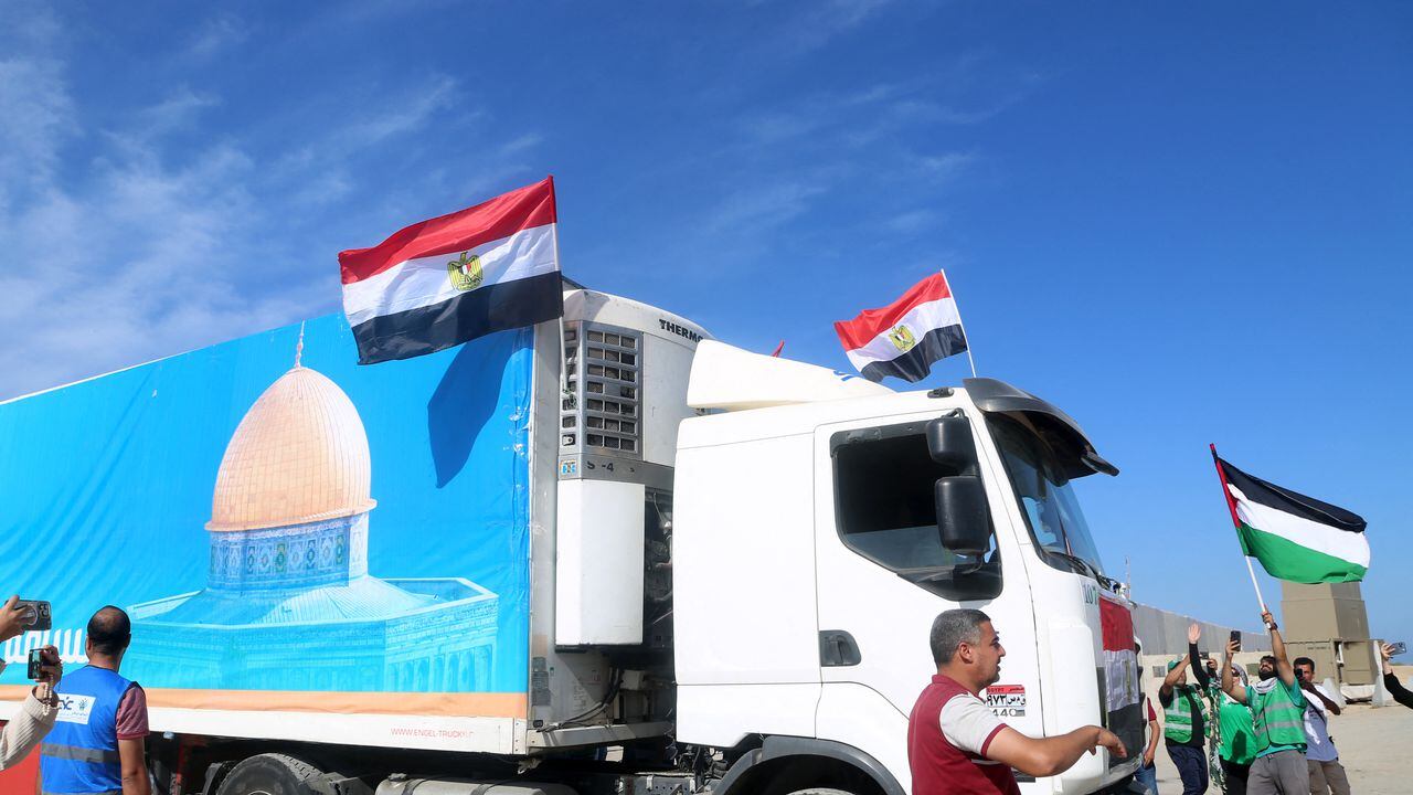 La gente en el lado egipcio del cruce fronterizo de Rafah aplaude mientras un convoy de camiones que transportan ayuda humanitaria cruza hacia la Franja de Gaza el 21 de octubre de 2023. El primero de 20 camiones que transportaban ayuda humanitaria entró en la Franja de Gaza asediada y devastada por la guerra el 21 de octubre.